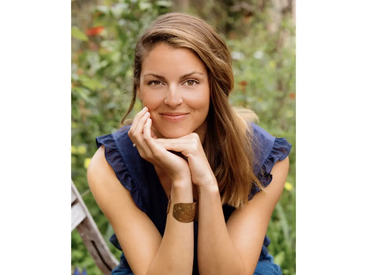 Woman smiling with hands on chin outdoors.