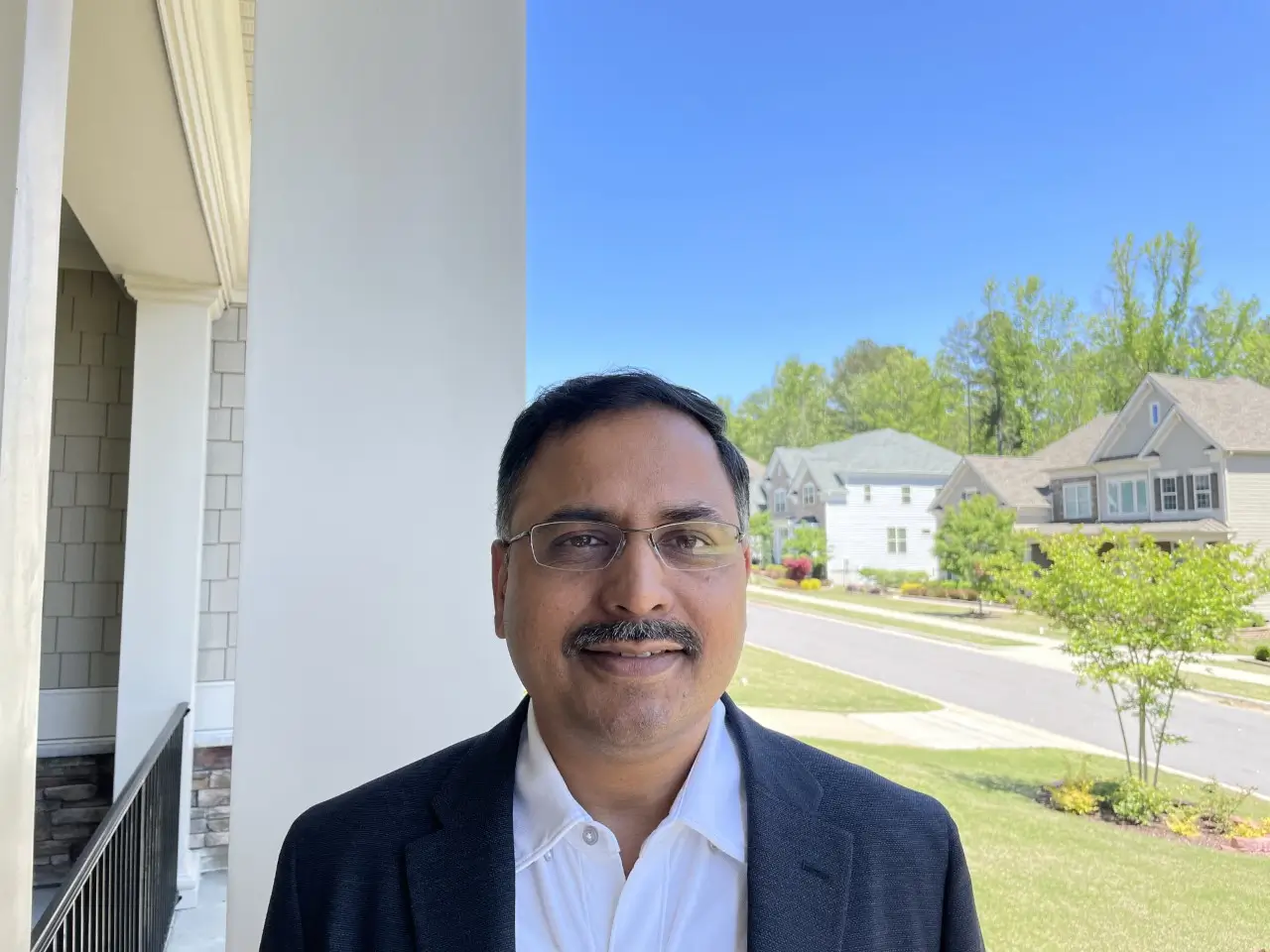 Man in a suit smiles outside a home.